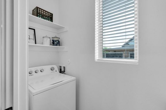 Bright laundry area with a washing machine and shelves on a white wall.